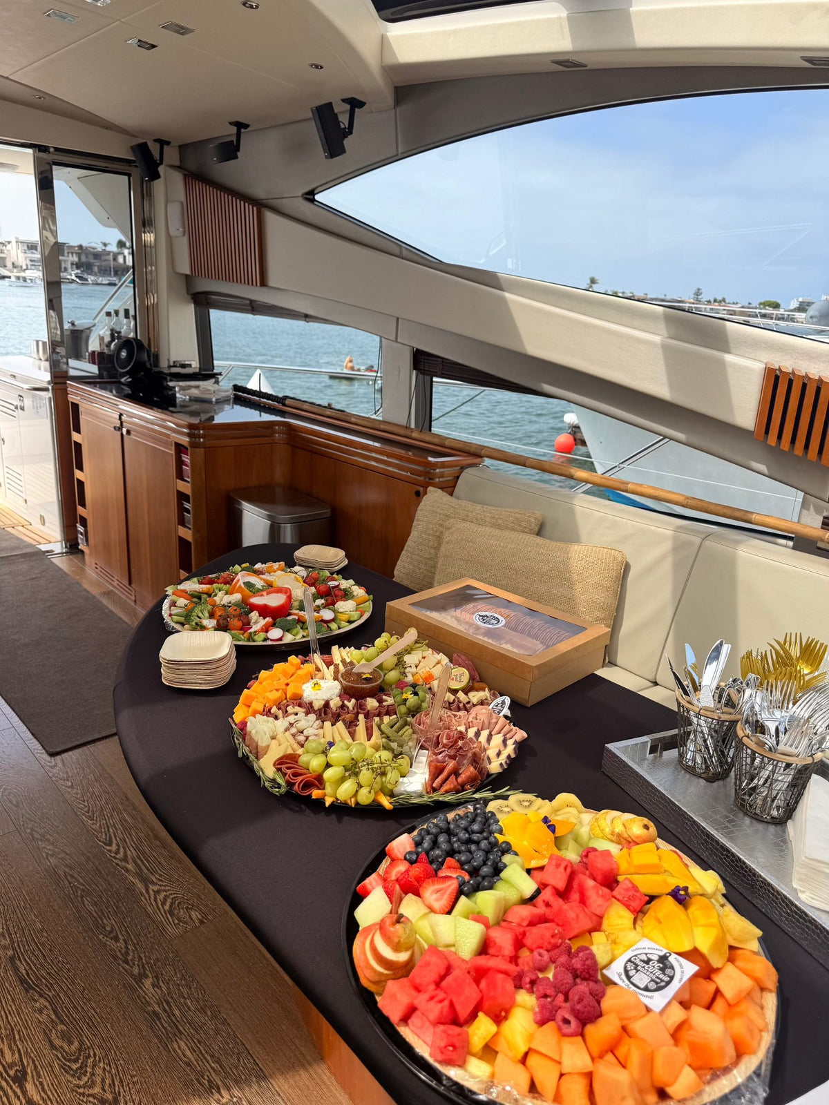 Luxury yacht galley with black serving table holding three large charcuterie and fruit platters for Newport Beach catering