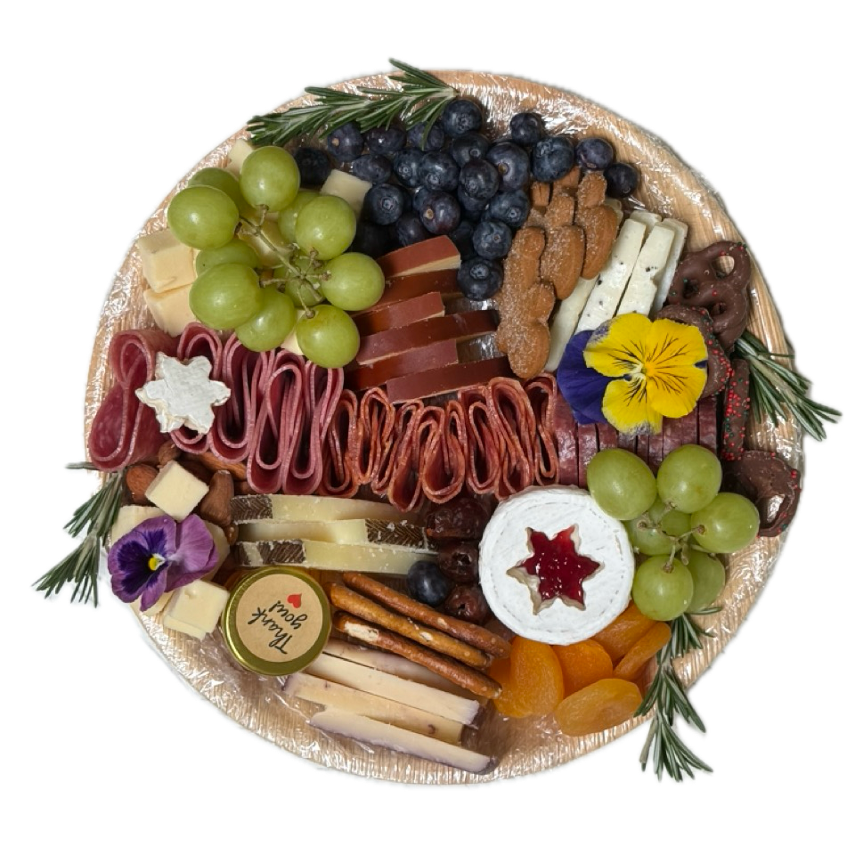 Large round charcuterie board covered in foil with sliced meats, cheeses, grapes and blueberries for Newport Beach delivery