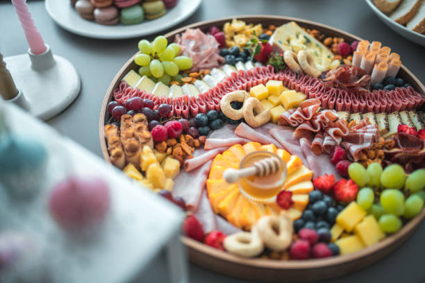 A round charcuterie board by OC Charcuterie Boards, filled with artisan cheeses, cured meats, fresh fruit, and crackers